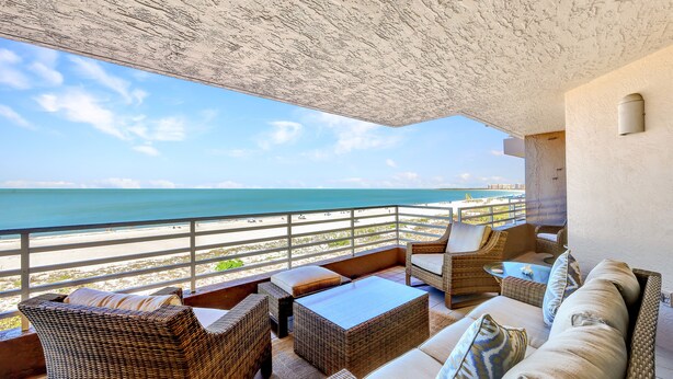 A balcony with wicker furniture overlooking a beach.