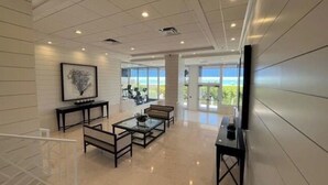 A spacious room with a large window offering a view of the outdoors, a seating area with tables, and a flat-screen TV mounted on the wall.