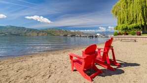 Una playa con dos sillas Adirondack rojas mirando un lago tranquilo, rodeada de vegetación y colinas distantes.