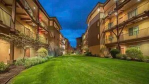 Un pasillo de hotel con un césped verde, varios balcones e iluminación cálida.