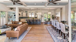 A spacious living area with a large sofa, a dining table with chairs, and a kitchen in the background. - Stollaway Retreat - 5 Bedrooms with Pool (St Simons Island)