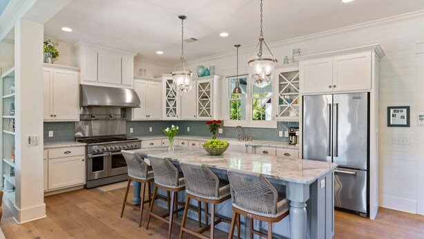 A modern kitchen with white cabinetry, stainless steel appliances, and a central island with bar stools. - Stollaway Retreat - 5 Bedrooms with Pool (St Simons Island)