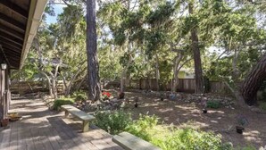 Une terrasse en bois avec un banc, entourée d’arbres et d’un jardin.
