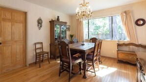 Une salle à manger avec une table et des chaises en bois, un lustre, un buffet et une fenêtre avec des rideaux.