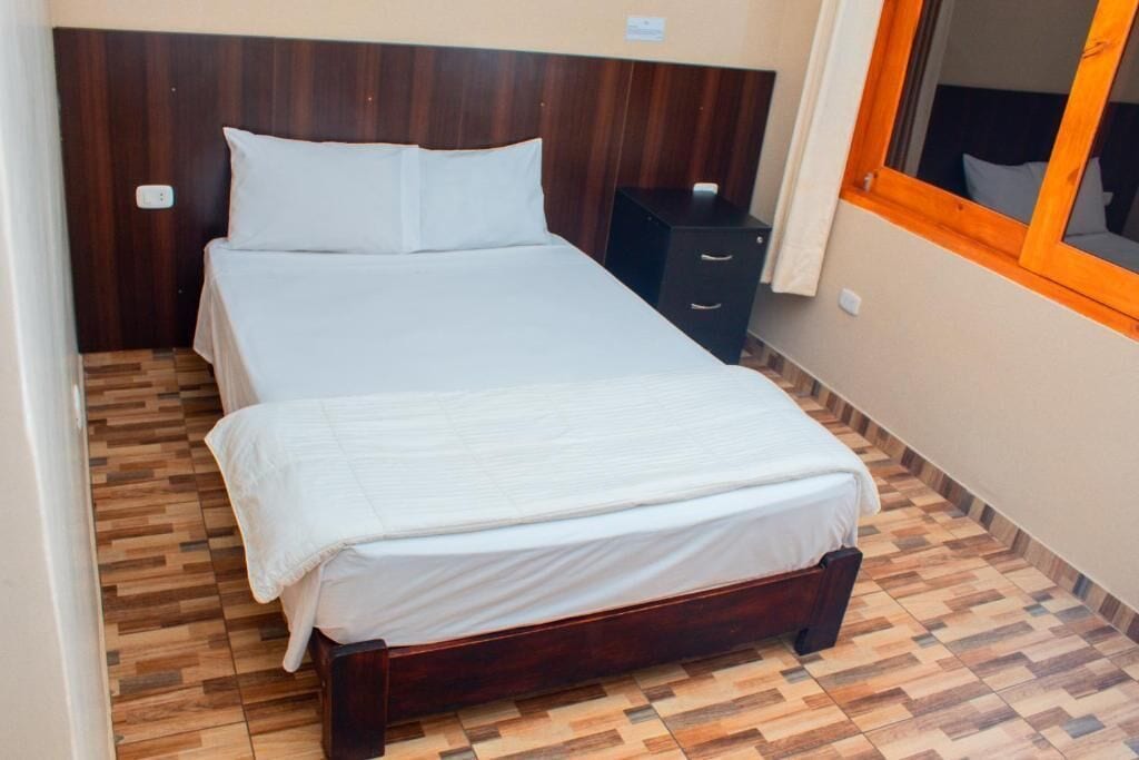 A small, neatly made bed with a wooden headboard and a wooden floor with a herringbone pattern.
