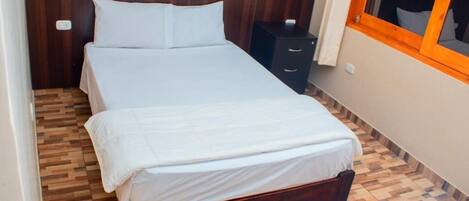 A small, neatly made bed with a wooden headboard and a wooden floor with a herringbone pattern.