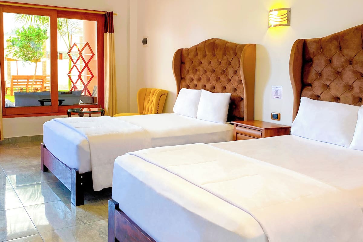 A hotel room with two beds, a chandelier, a sliding glass door leading to an outdoor area, and a small table with a chair.