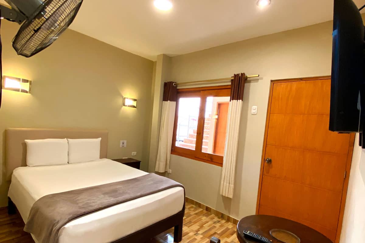 A hotel room with a bed, a desk, a chair, a TV, and a window with curtains.