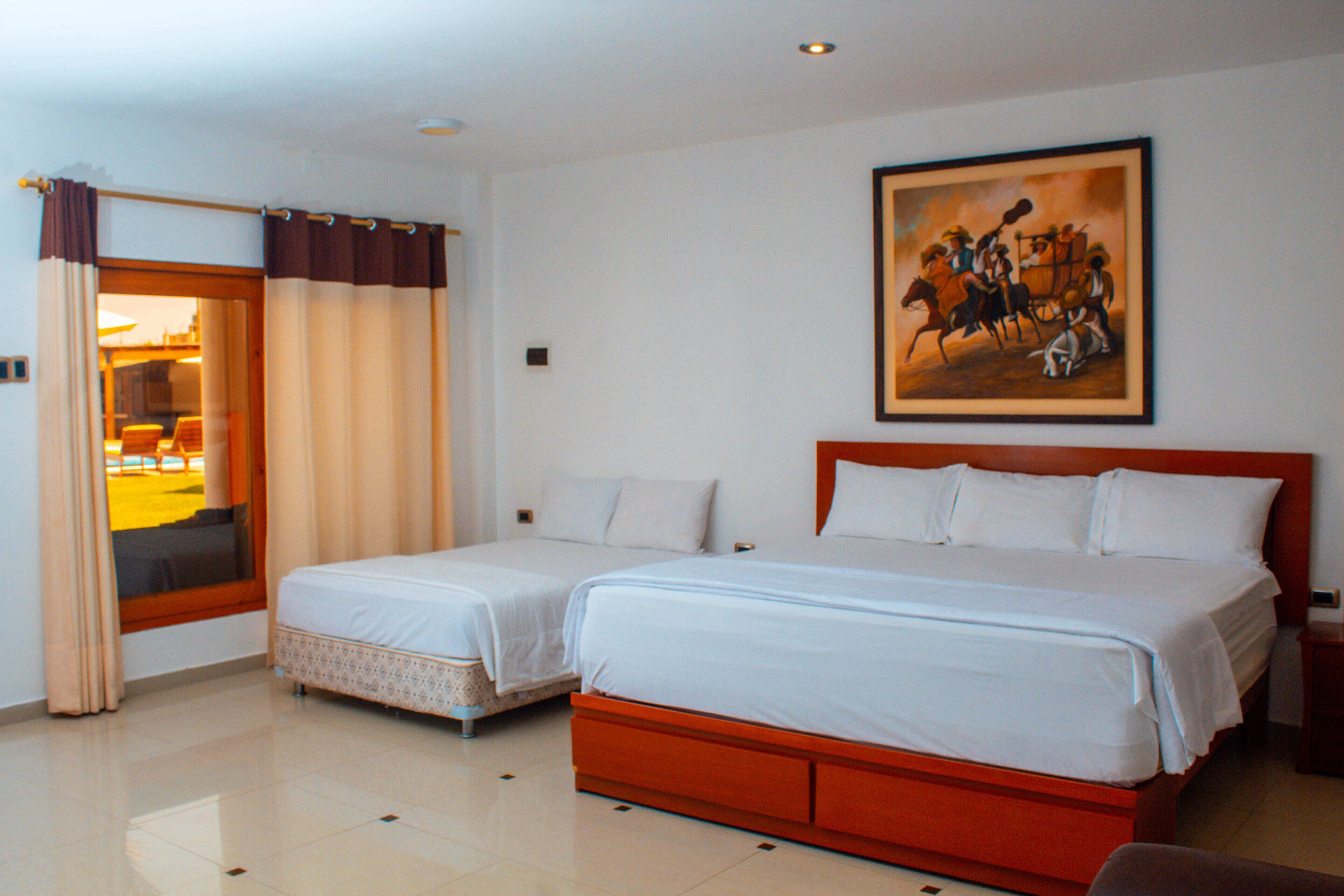 A hotel room with two beds, a painting on the wall, and a view through the door.