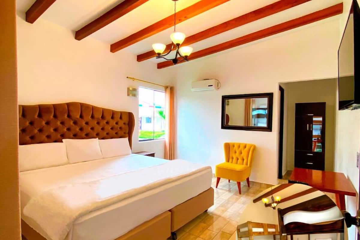 A bedroom with a large bed, a yellow armchair, a bunk bed, and a wooden ceiling.