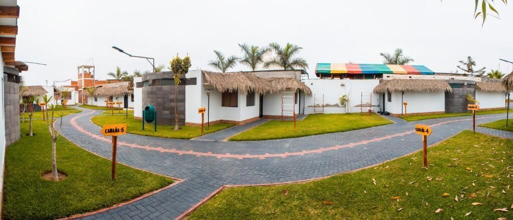 A resort with thatched-roof huts, paved pathways, and a central building with a colorful roof.