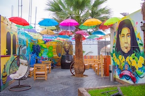 A vibrant outdoor seating area with colorful umbrellas, a mural, and a palm tree.