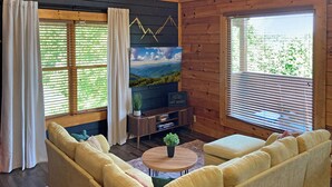 A cozy cabin interior with a sofa set, a coffee table, a TV, and a fireplace.