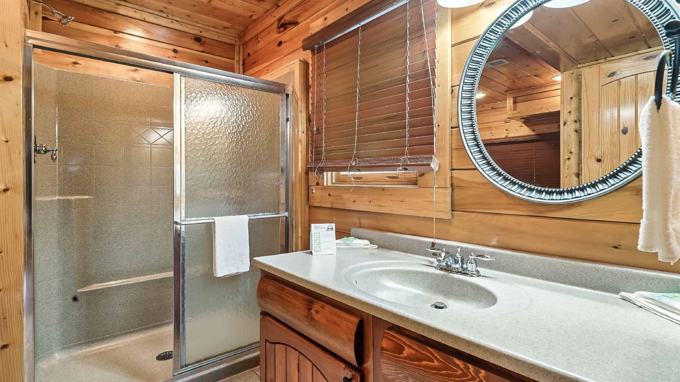 Een houten badkamer in een chalet, met een glazen douche, een wastafel en een spiegel.