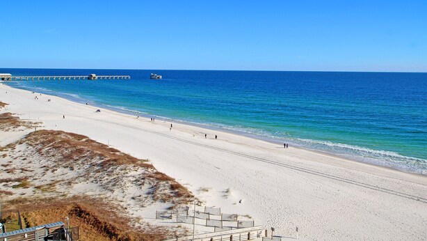A beach with a long stretch of sand, a pier extending into the water, and a clear blue sky. - Gulf Shores Condo Clearwater 8C | Sleeps 6 (Gulf Shores)