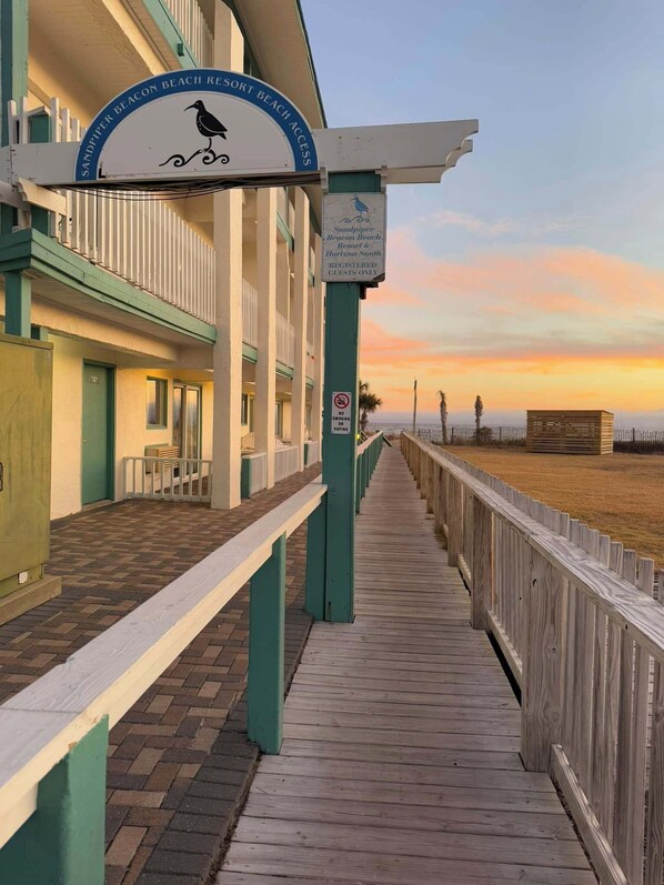 A wooden boardwalk leading to a building with a sign indicating it is part of Sandpiper Beacon Beach Resort & Horizon South.