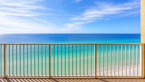 Ein Balkon mit Blick auf ein klares, blaues Meer und einen Sandstrand.