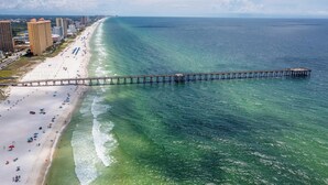 A beach with a long pier extending into the ocean, surrounded by buildings and a clear sky. - Summer Towne cottage w/ pool and beach access (Panama City Beach)
