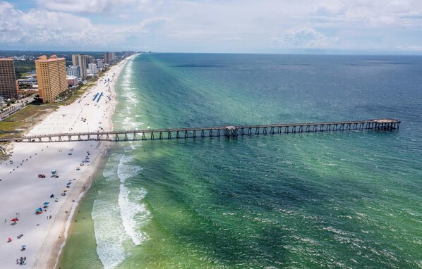 A beach with a long pier extending into the ocean, surrounded by buildings and a clear sky. - Summer Towne cottage w/ pool and beach access (Panama City Beach)