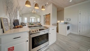 A modern kitchen with white cabinetry, a built-in oven, and a central island with a stove. There are pendant lights above the island and a chandelier on the ceiling. - Summer Towne cottage w/ pool and beach access (Panama City Beach)