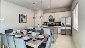 A modern kitchen with white cabinets, stainless steel appliances, and a dining area with a wooden table and grey chairs.