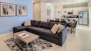 A modern living room with a sectional sofa, a coffee table, and a dining area with a kitchen in the background.