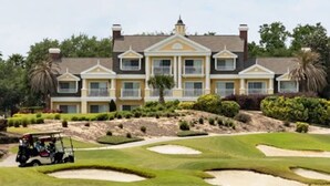 A golf course with bunkers and a golf cart, and a large building with a symmetrical facade in the background.