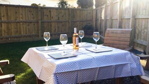 Une table dressée à l’extérieur, recouverte d’une nappe à motifs, avec quatre verres à vin et une bouteille de vin.
