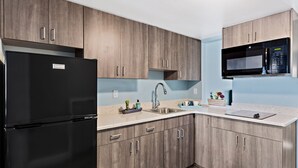 Een moderne keuken met houten kastjes, een zwarte koelkast, een roestvrijstalen spoelbak en een magnetron.