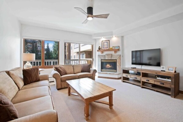 A spacious living room with a fireplace, a large flat-screen TV, and a ceiling fan. - Saint James Place 116 (Beaver Creek)