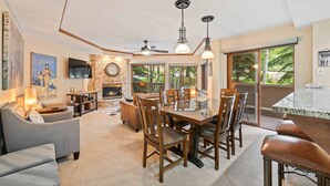 Un salon spacieux doté d’une cheminée, un coin repas avec une table à plateau en verre et une grande fenêtre offrant une vue sur l’extérieur.