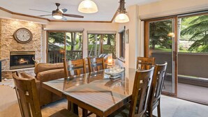 Un espace repas comprenant une table en verre, des fauteuils en cuir, une cheminée et de grandes fenêtres donnant sur l’extérieur.