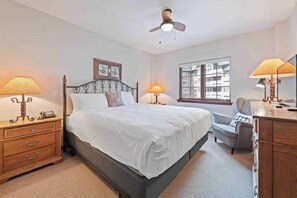 Ein Schlafzimmer mit einem Bett, Nachttischlampen, einem hölzernen Nachttisch, einem Schreibtisch, einem Stuhl und einem Deckenventilator.