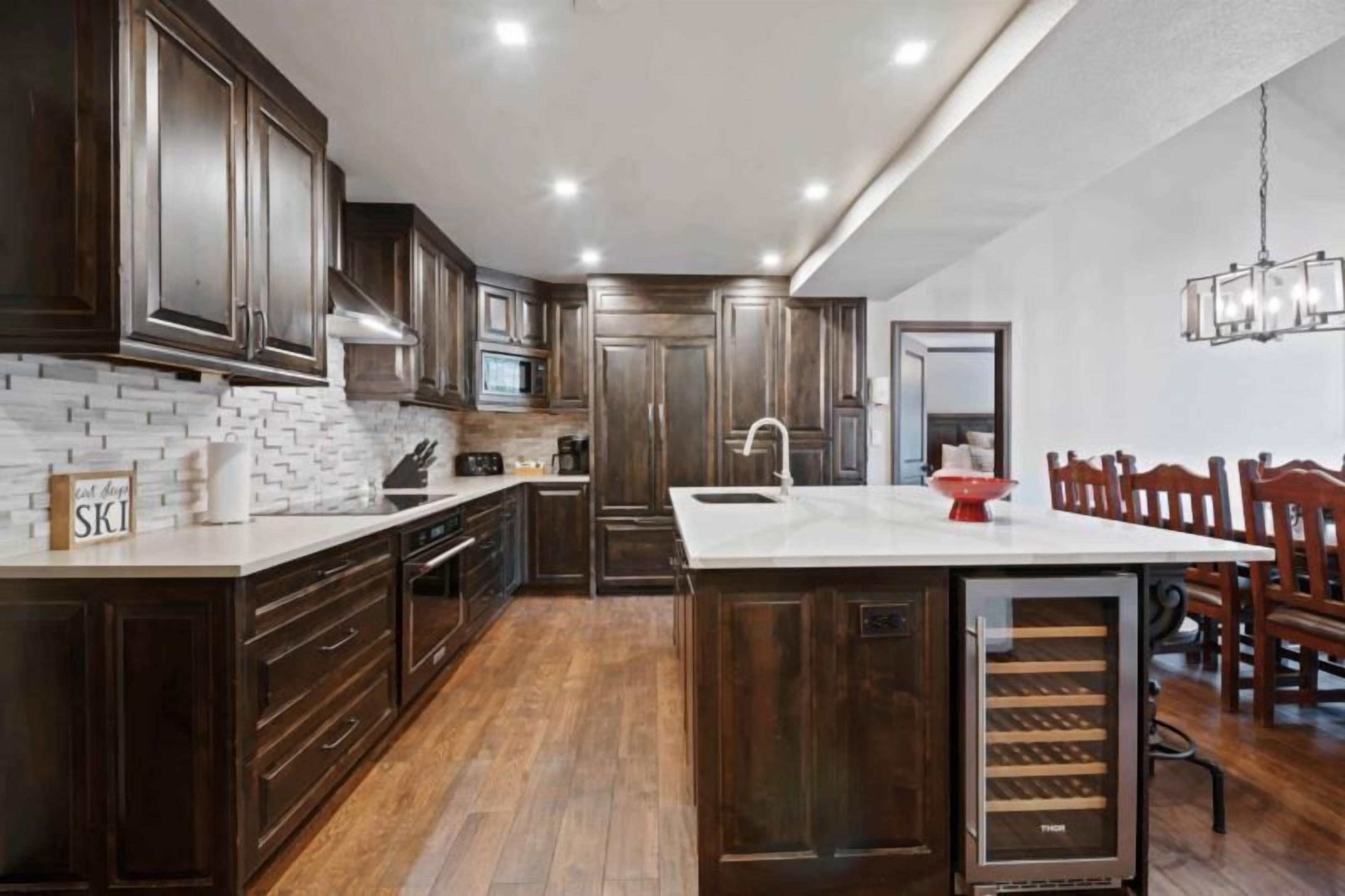 A modern kitchen with dark wood cabinets, a white countertop, and a built-in wine cooler.