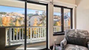 Un balcón con vistas a árboles otoñales y casas, una silla y una cesta con objetos.