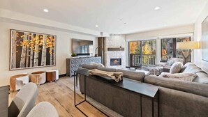 Una sala de estar moderna con chimenea, un sofá grande y un comedor con cocina al fondo.