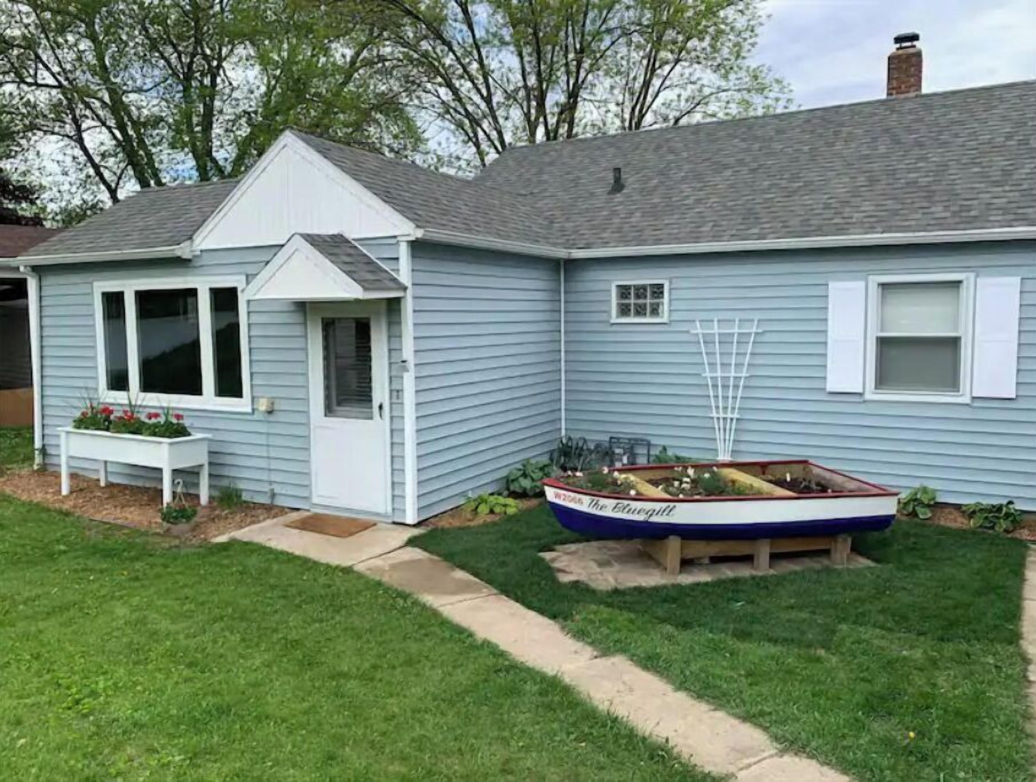 Une maison avec un petit jardin, un banc blanc et un jardinier en forme de bateau.