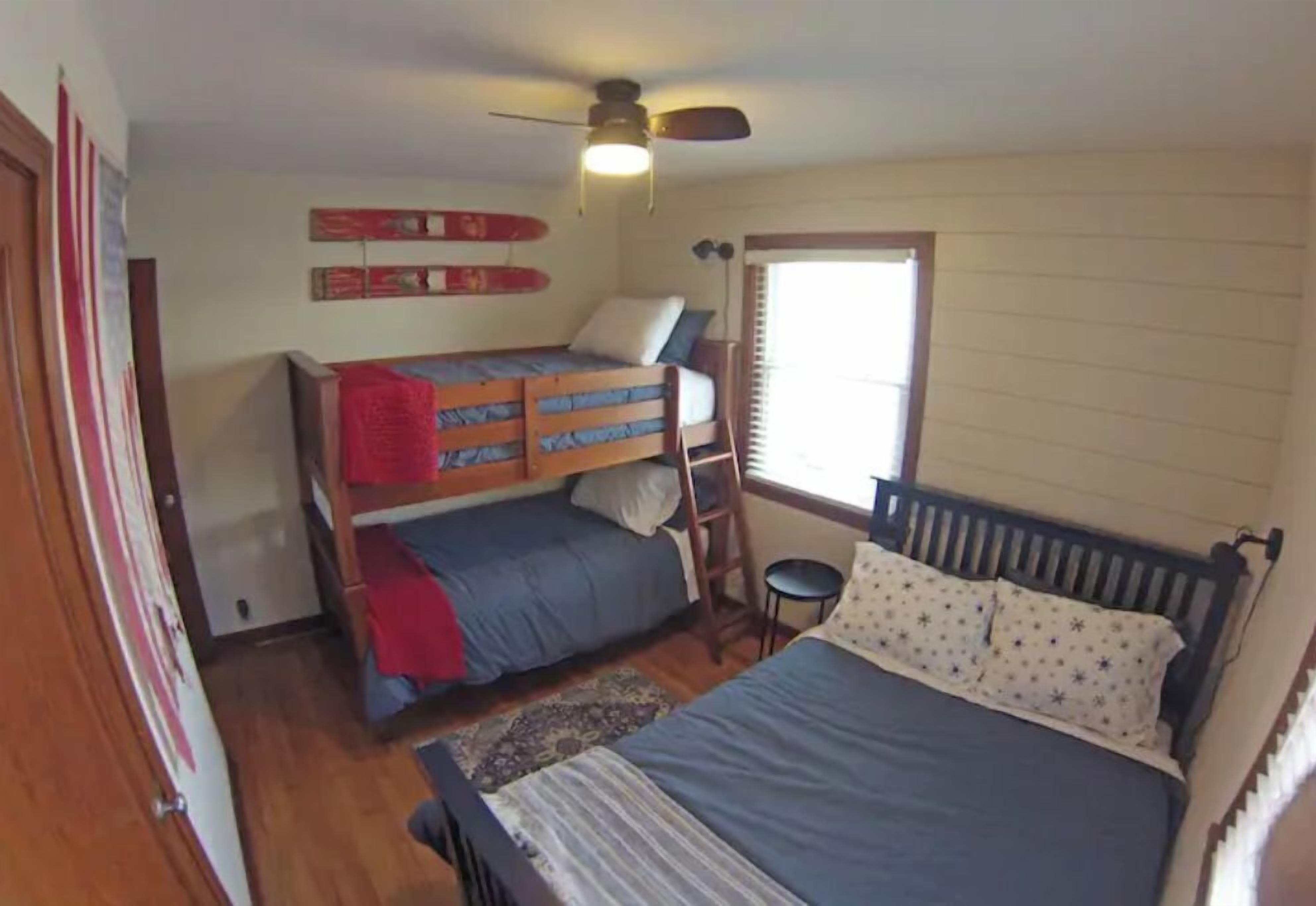 A bedroom with a bunk bed, a single bed, a ceiling fan, and a window with blinds.