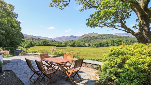 A patio with a round table and four chairs, overlooking a lush green valley and distant mountains. - Spindle Coppice (Ambleside)