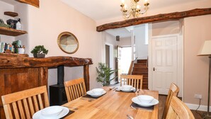 A dining area with a wooden table set for four, surrounded by wooden chairs. A mirror hangs on the wall above the table, and a chandelier is visible above. - Spindle Coppice (Ambleside)