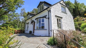 A white two-story house with a stone pathway leading to the entrance, surrounded by greenery. - Spindle Coppice (Ambleside)