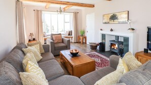 A cozy living room with a fireplace, wooden beams, a sofa set, and a window seat. - Spindle Coppice (Ambleside)