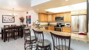 A modern kitchen with wooden cabinets, a stainless steel refrigerator, and a granite countertop. - Renovated Beachwalk 3 Bedroom Condo -5 minute walk to Beach! (Naples)