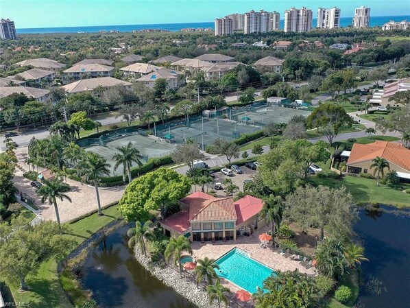 Vue aérienne d’un quartier résidentiel avec une grande piscine, des courts de tennis et une maison au toit rouge.
