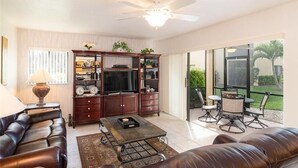 A spacious living room with a leather sofa, a coffee table, and a TV stand. There is a balcony with outdoor furniture. - Renovated Beachwalk 3 Bedroom Condo -5 minute walk to Beach! (Naples)