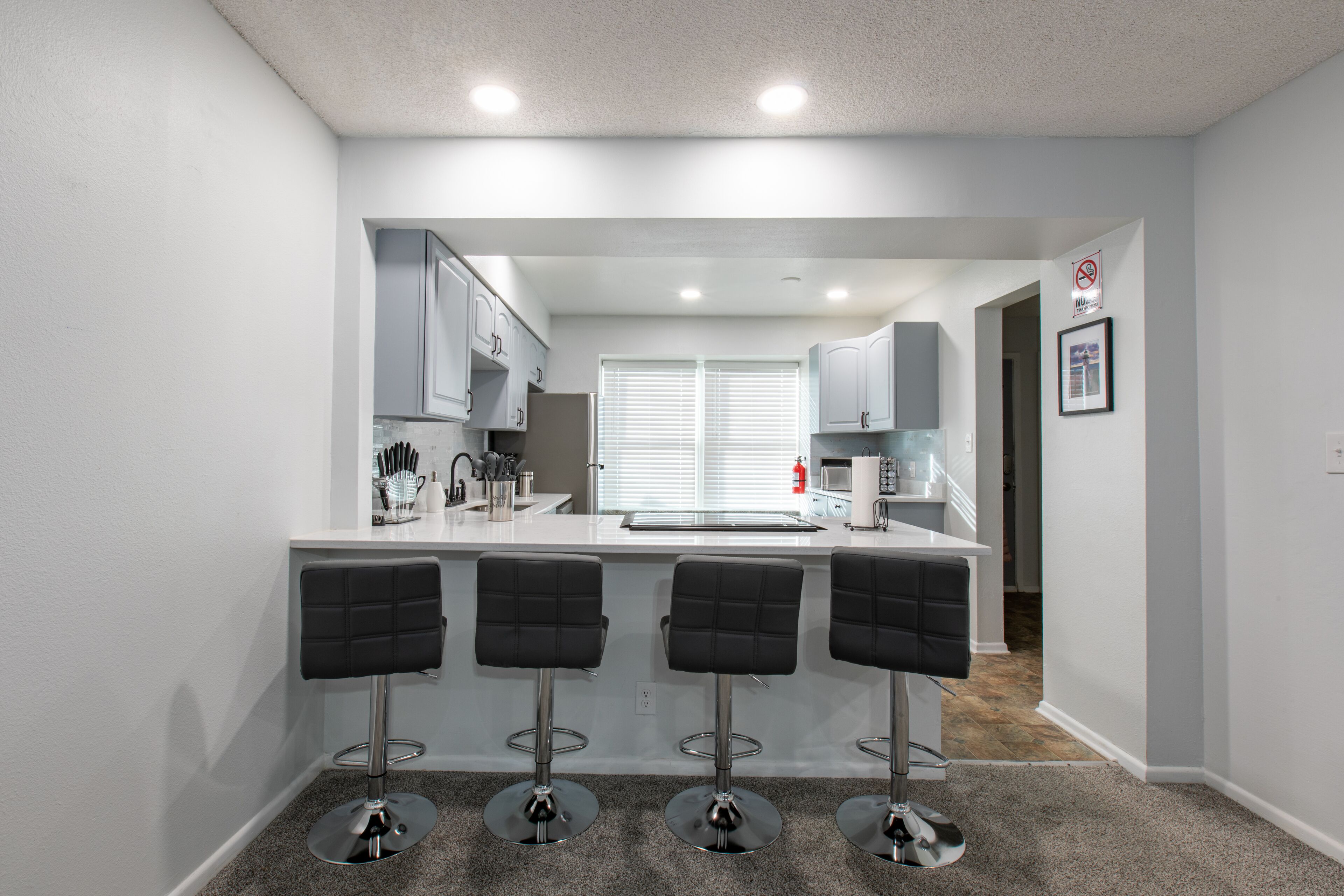 A modern kitchen with white cabinets, a central island with bar stools, and a window with blinds.