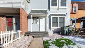 A two-story house with a front porch, a mailbox, and a small garden area with snow. - Charming 4-bedroom Townhouse  25 min from Denver (Northglenn)