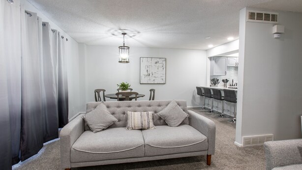 A living room with a grey sofa, a dining table with chairs, a kitchen area, and a ceiling light fixture. - Charming 4-bedroom Townhouse  25 min from Denver (Northglenn)