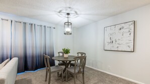 A dining area with a round table, four chairs, a hanging light fixture, a potted plant, and a large abstract painting on the wall. - Charming 4-bedroom Townhouse  25 min from Denver (Northglenn)