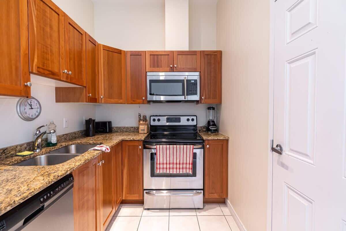 A kitchen with wooden cabinets, a microwave, an oven, a dishwasher, and a clock on the wall.